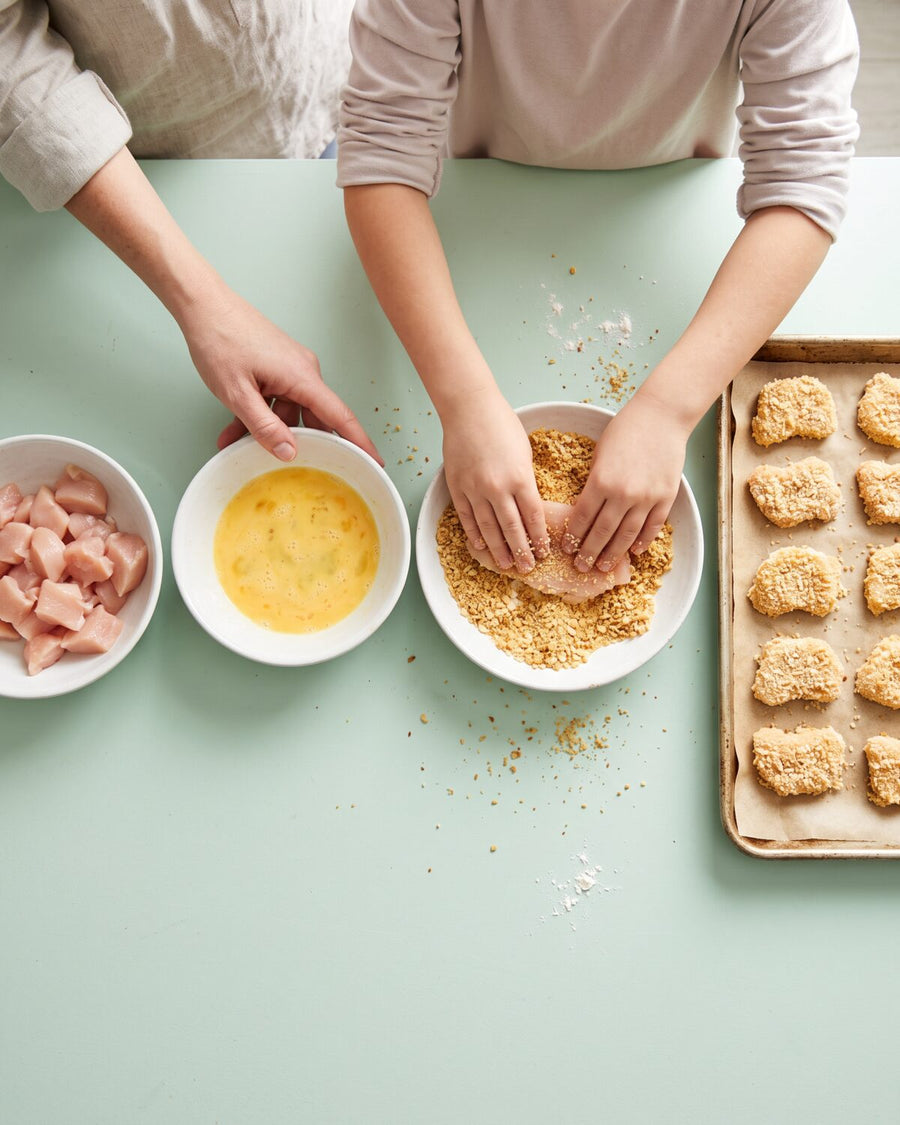 A child presses chicken into breadcrumbs next to a tray of nuggets